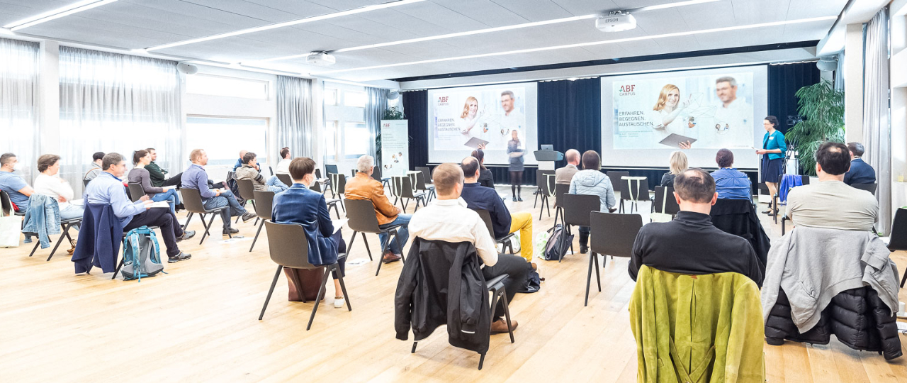 Personen sitzen in Konferenzraum und sehen eine Präsentation